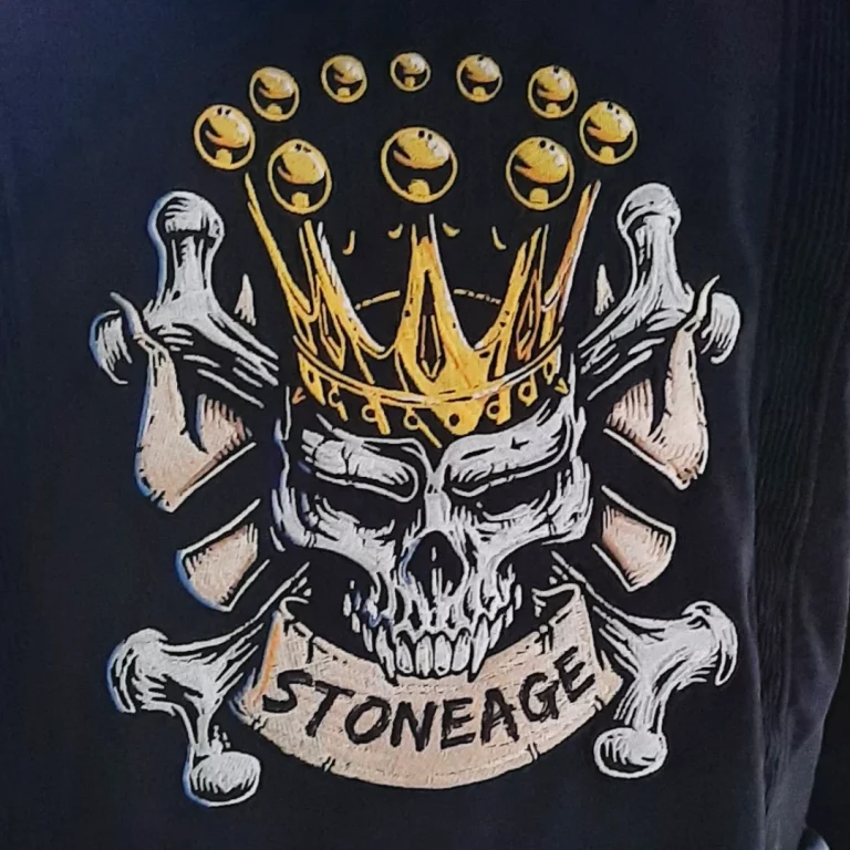 Stickerei eines Totenschädels mit Krone. Im Mund Hält es ein Banner mit "Stoneage"