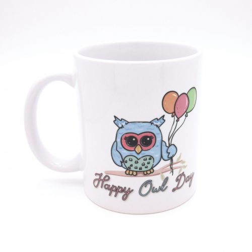 Auf dem Foto ist eine weiße Kaffetasse mit niedlicher kleinen Eule zu sehen. Die Eule ist hellblau mit grünem Bauch und rötlichen Augenumrandung. Die Eule hält drei verschiedenfarbige Luftballons in der Hand: orange, rot und grün. Die kleine Eule sitzt auf einem Ast. Unter dem Ast steht "Happy Owl Day"