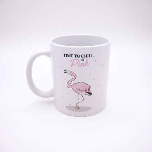 Das Foto zeigt eine weiße Tasse mit einem gezeichneten pinken Flamingo, der auf einem Bein steht. Darüber die Aufschrift "Time to chill in pink". Das Pink ist in Flamingofarben. Die restliche schrift ist schwarz. Auf der Tasse un um den Flamingo herum sind viele kleine pinke Sterne.