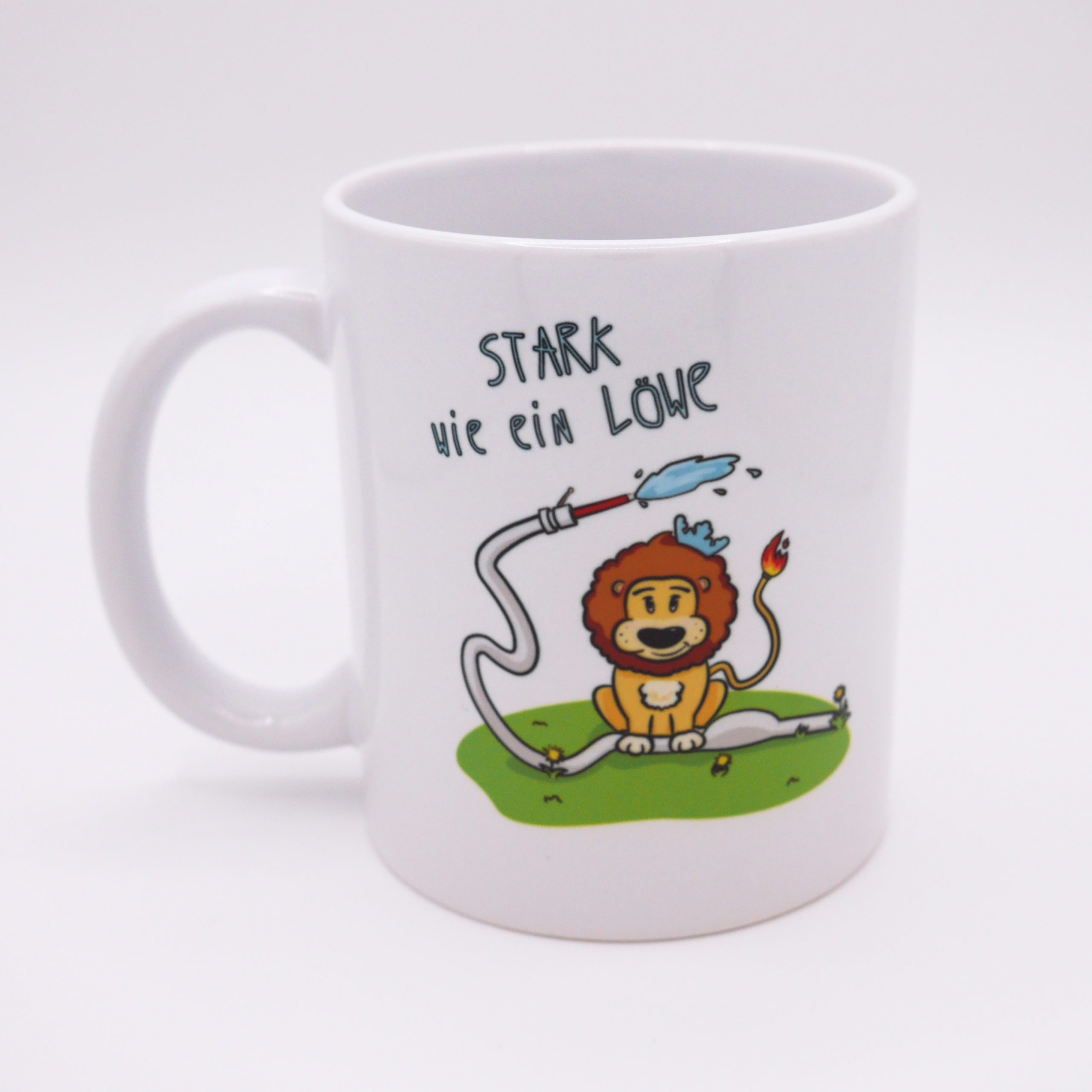 Auf dem Foto ist eine weiße Kaffeetasse zu sehen. Auf der Tasse ist ein kleiner niedlicher Feuerwehr-Löwe. Der Löwe ist orange mit brauner Mähne. Er trägt eine blaue kleine Krone und hat einen Schwanz mit Feuer-Schweif. Der Löwe steht auf einem Feuerwehrschlauch, der durch die gegend wirbelt und aus dem Wasser Spritzt.