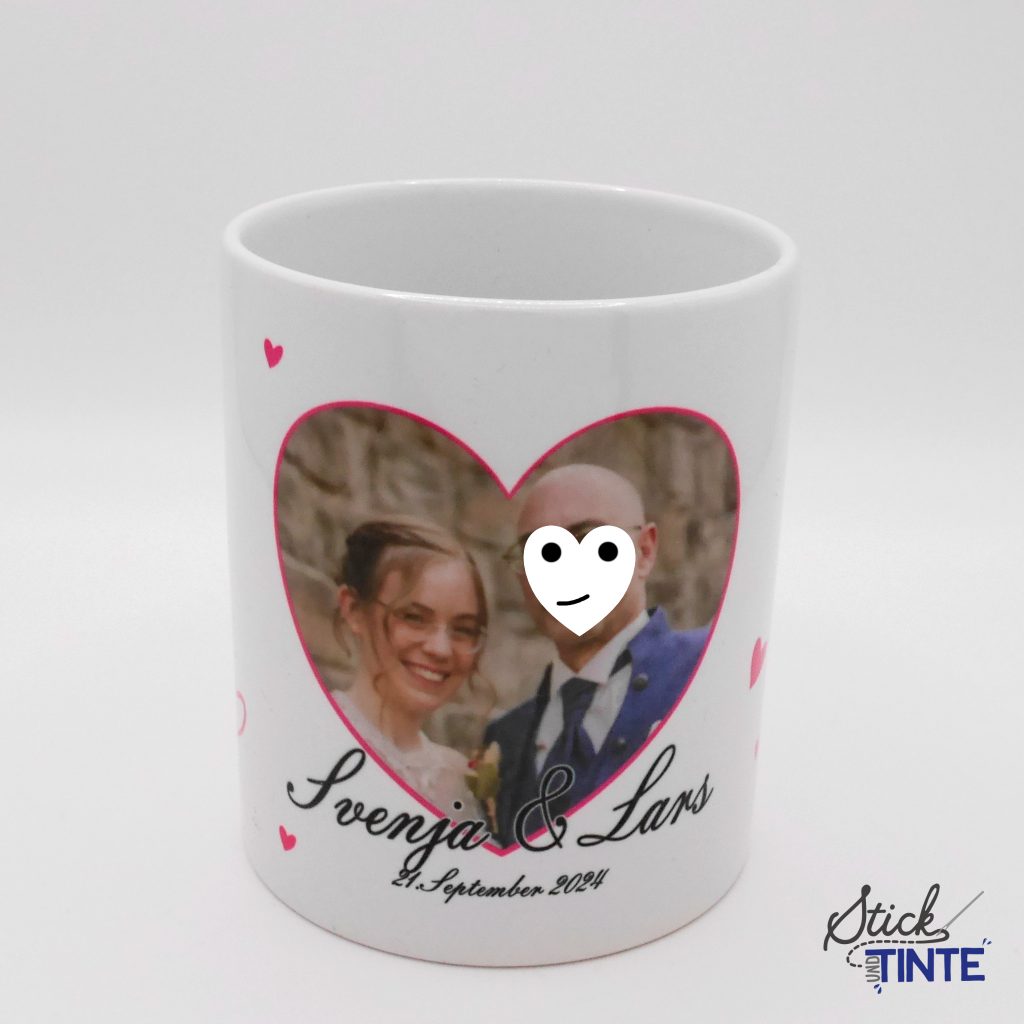 Das Bild zeigt eine Tasse mit Fotoaufdruck. Das Foto ist in einem pinkfarbigem Herz eingerahmt und zeigt ein Hochzeitspaar. Datunter sind Namen und Hochzeitsdatum.