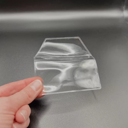 Transparente Schutzhülle bzw. Aufbewahrungshülle für Brillenputztücher, hier gehalten von einer Hand. Hintergrund schwarz/antrazit