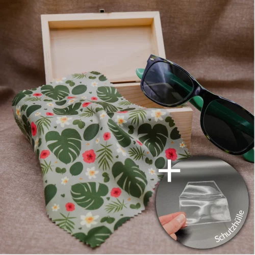 Micrfofastertücher für Brillen und Displays, mit Urban Jungle Muster: Monstera-Blätter, Blätter verschiedener Grünpflanzen und Dschungelblumen. Das Tuch liegt hier auf kleinen Schatzkiste. Es hängt halb herunter. An die Schatzkiste angelehnt ist auch eine grüne Sonnenbrille. Der Hintergrund ist brauner Leinenstoff